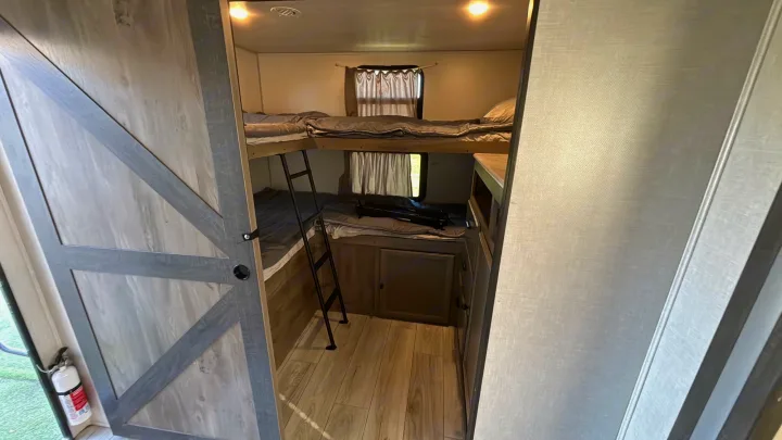 View of the bunkhouse in an RV rental, featuring two beds, a ladder, storage, and a fire extinguisher for safety.. Forest River Surveyor Legend 2023