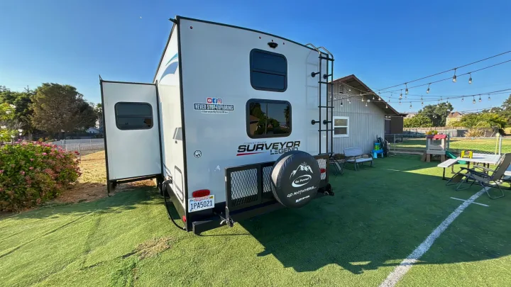 Explore this Forest River Surveyor Legend travel trailer. An excellent RV rental option, it's parked with its slide-out extended in a green backyard.. Forest River Surveyor Legend 2023