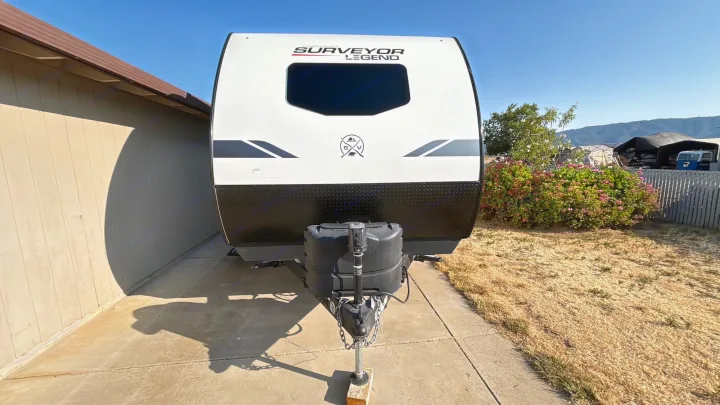 Front view of a white and black Surveyor Legend travel trailer, parked on a sunny driveway, perfect for rv rental trips.. Forest River Surveyor Legend 2023