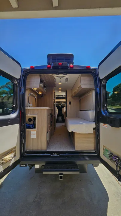 Inside an RV rental: rear doors open, revealing a modern interior with a kitchen, living space, and wood accents.. Entegra Coach Ethos 2024