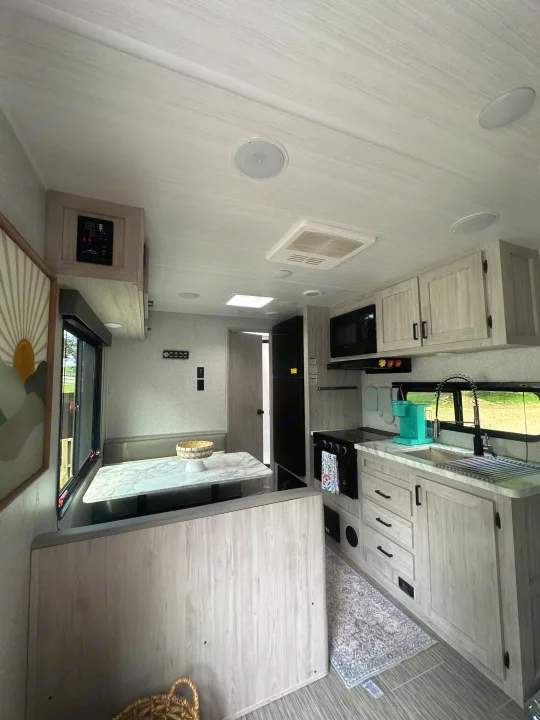 Modern RV rental interior with kitchen and dining area. Features light wood cabinetry & appliances for comfy travel.. East to West Silver Lake 2023