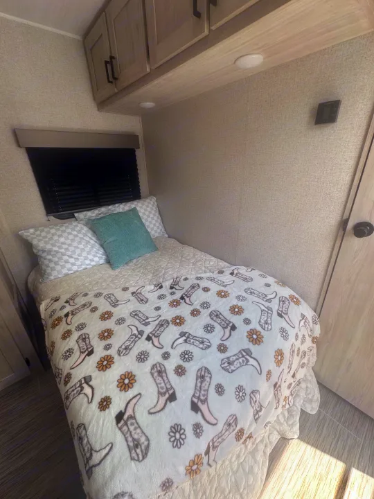 Inviting RV rental bedroom with a bed featuring a fun cowboy boot blanket, checkered pillows, and built-in cabinets.. East to West Silver Lake 2023