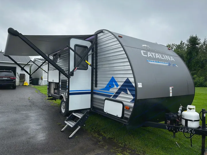 This sleek grey travel trailer with an extended awning is ready for your next rv rental adventure, parked on a wet driveway.. Coachmen Catalina 2022