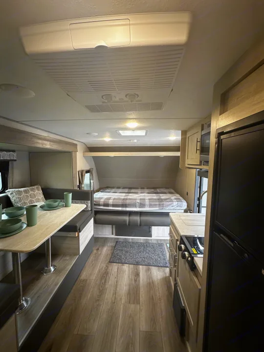 Inside this cozy rv rental: a dining area with green dishes, a comfortable bed, and a compact kitchen. Ideal for your trips.. Coachmen Catalina 2022