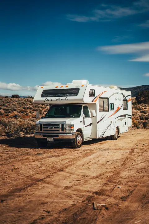A white Four Winds RV rental is parked on a dirt road under a clear blue sky, with arid brush in the background.. Four Winds Four Winds Motorhome 2011