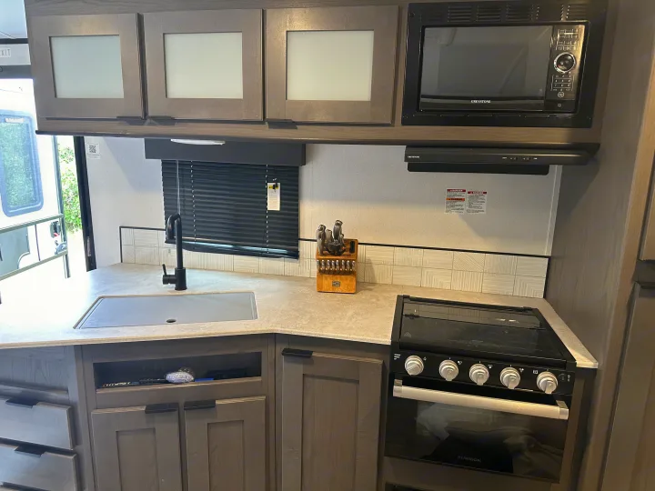 This **rv rental** interior features a modern kitchen with a sink, microwave, oven, and sleek grey cabinets, perfect for compact living.. Mpg 2500BH MPG 2021