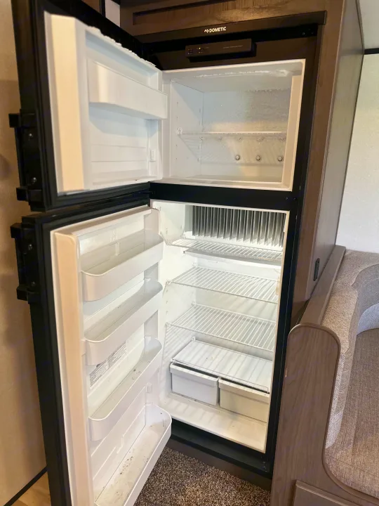 RV rental: An open, empty Dometic RV refrigerator/freezer combo, with some frost in the top section.. Mpg 2500BH MPG 2021
