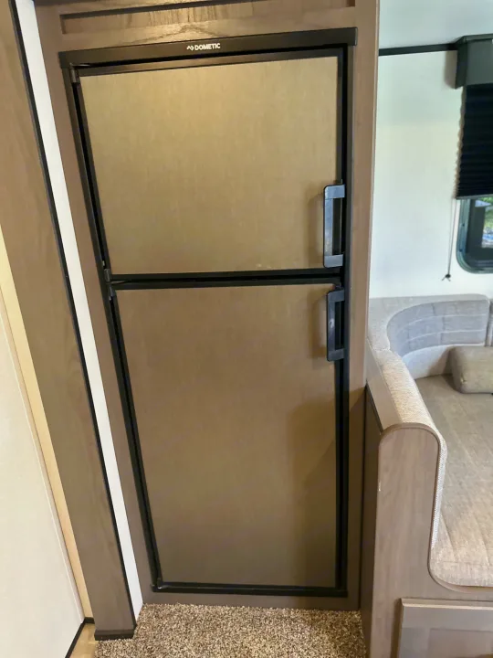 A Dometic refrigerator with top freezer in an RV rental. Its beige doors and black handles offer essential onboard storage.. Mpg 2500BH MPG 2021