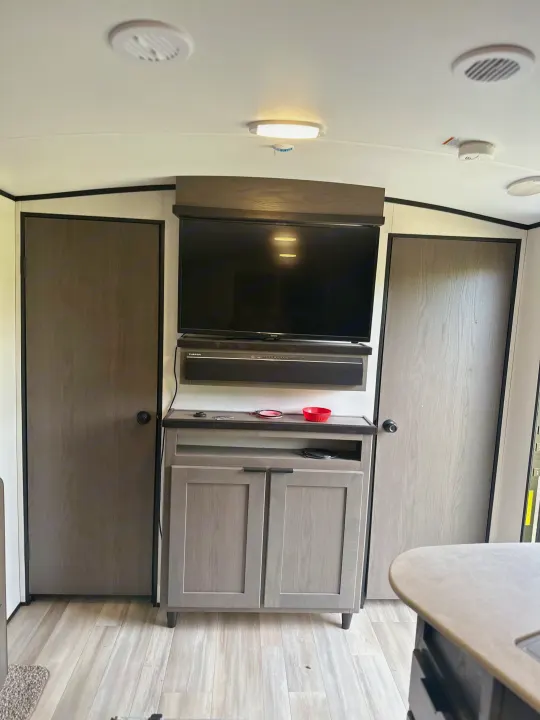 Modern RV rental interior: TV, soundbar, storage cabinet, and two doors, with ceiling lights and vents.. Mpg 2500BH MPG 2021