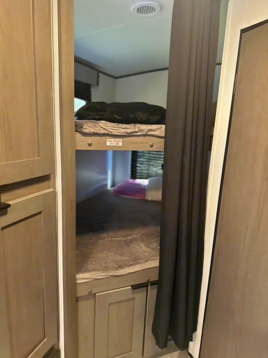 Interior of an RV rental showing stacked bunk beds with a weight limit, privacy curtains, and wooden cabinetry.. Mpg 2500BH MPG 2021
