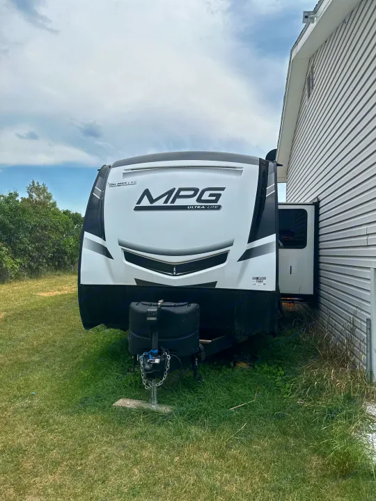 Front view of a white MPG Ultra-Lite travel trailer RV parked on grass beside a house, ready for your next rv rental getaway.. Mpg 2500BH MPG 2021