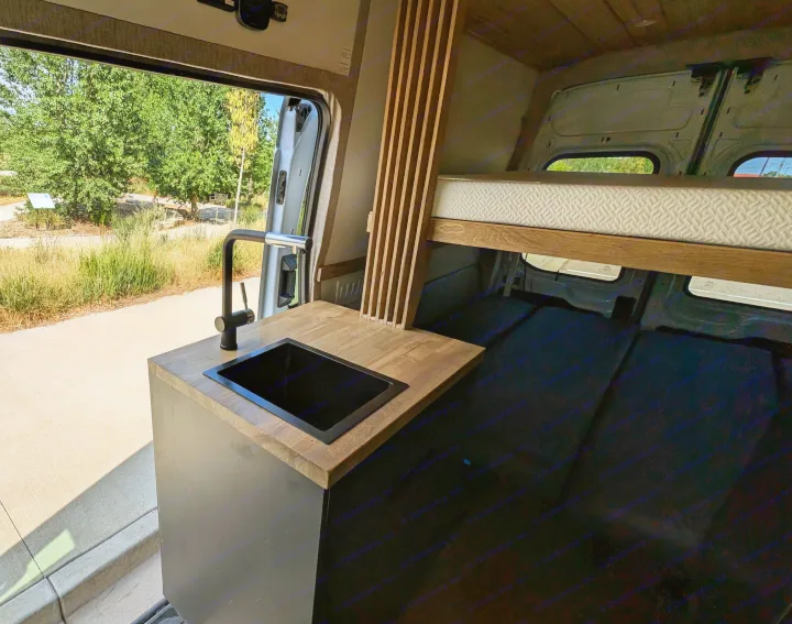 Experience van life in this RV rental! Modern camper interior with kitchen, elevated bed, and open door to scenic outdoors.. Ford Van 2024