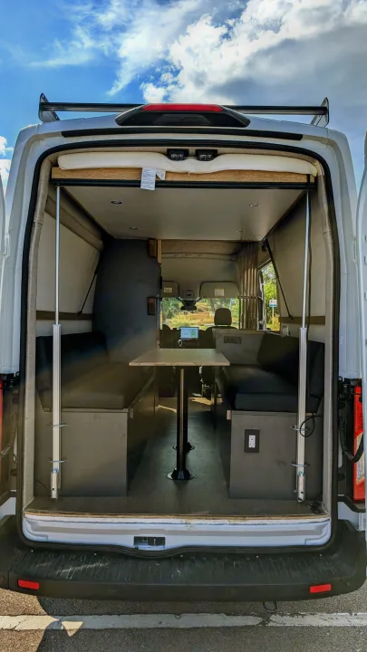 View inside an RV rental's cozy camper van conversion from open rear doors, showing dinette and bed setup.. Ford Van 2024