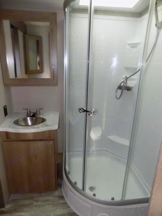 Compact RV rental bathroom showcasing a corner glass shower, vanity with sink, and framed mirror for convenience.. Grand Design Imagine 2023