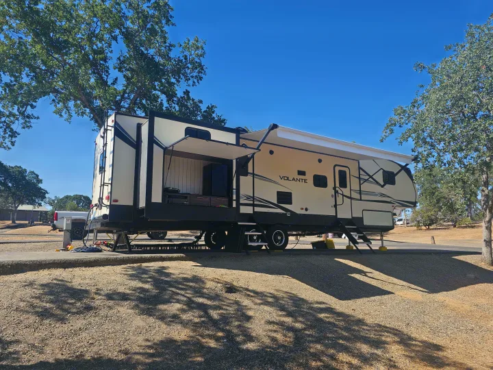 A modern travel trailer RV rental, featuring an open outdoor kitchen, is parked at a sunny campground.. Crossroads RV Volante 2019