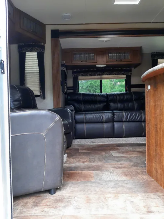 Spacious RV rental interior featuring dark leather recliners, wood-look flooring, overhead cabinets, and large windows with blinds.. Crossroads RV Zinger 2017