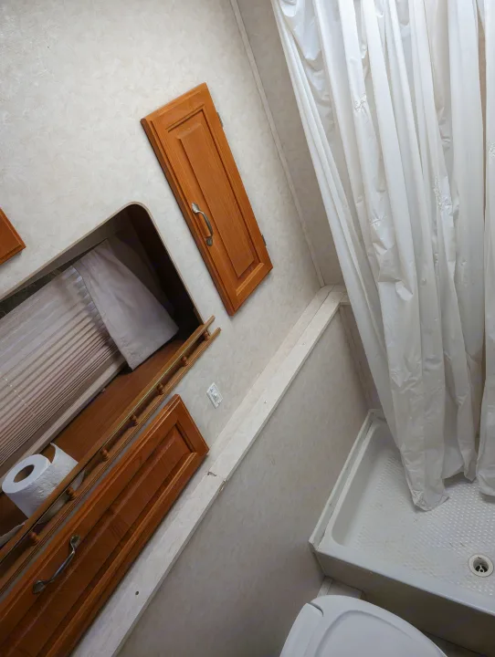 View inside a compact RV rental bathroom: white shower curtain, toilet, and wooden vanity with a toilet paper roll.. Hi Lo 2307c 2007