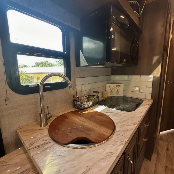 Inside an RV rental, a bright kitchen with marble-patterned counters, a sink, microwave, and a large window.. Jayco Melbourne 2022