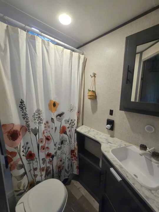 A clean RV rental bathroom with a vibrant floral shower curtain, toilet, and vanity featuring a sink and mirror.. Aspen Trail LE 2021