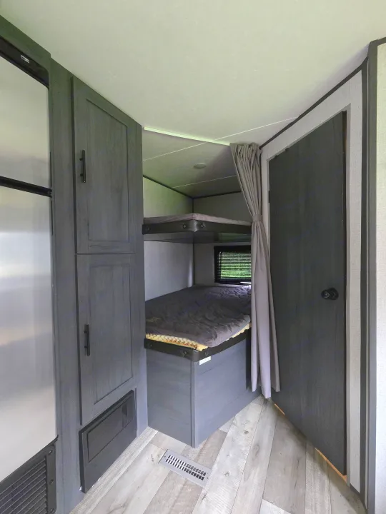 RV rental interior featuring bunk beds with a privacy curtain, adjacent storage, and modern wood-look flooring.. Aspen Trail LE 2021