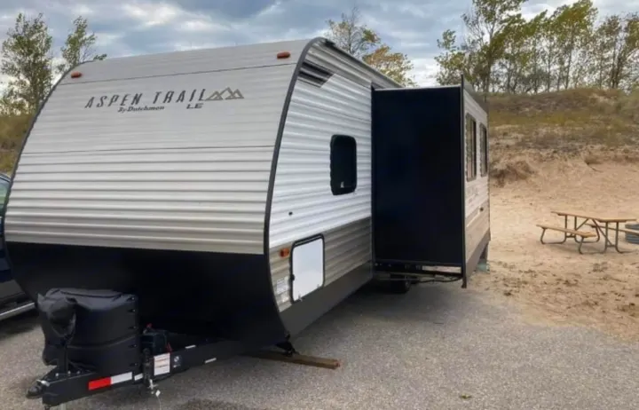 Gray Aspen Trail travel trailer RV rental with extended slide-out, parked at a sandy campsite.. Aspen Trail LE 2021