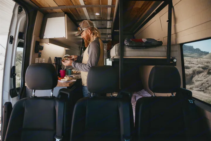 RV rental interior: A man preparing food in a cozy camper van kitchen with bunk beds & desert views.. Mercedes Mercedes Benz Sprinter Custom Van Conversion 2020