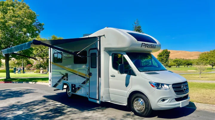 Experience freedom with this Class C rv rental, a sleek grey Coachmen Prism parked outdoors with its awning extended under a blue sky.. Coachmen Prism 2024