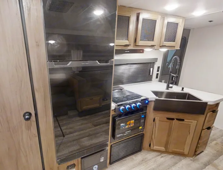 Modern RV rental kitchen with black refrigerator, gas stove, microwave, farmhouse sink, and light wood cabinetry.. Forest River Cherokee Grey Wolf 2022