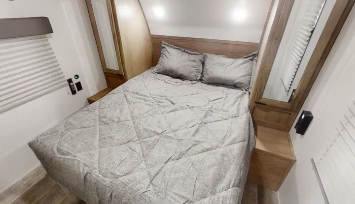 This RV rental bedroom features a queen bed with gray bedding, built-in wooden storage, and window blinds, ready for your trip.. Forest River Cherokee Grey Wolf 2022