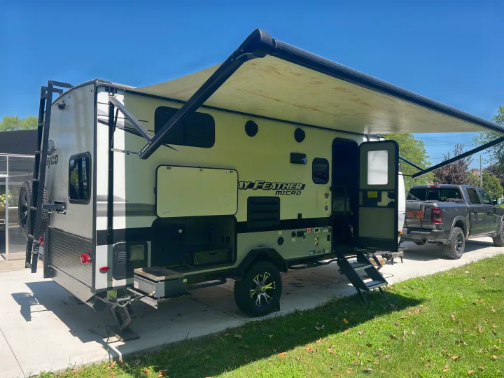 This RV rental travel trailer offers an extended awning, open door, and outdoor grill, parked with a pickup for camping.. Jayco Jay Feather Micro 2022