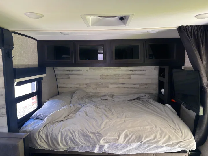 Cozy RV rental bedroom interior with a comfortable bed, overhead cabinets, window blinds, and a mounted TV.. Jayco Jay Feather Micro 2022