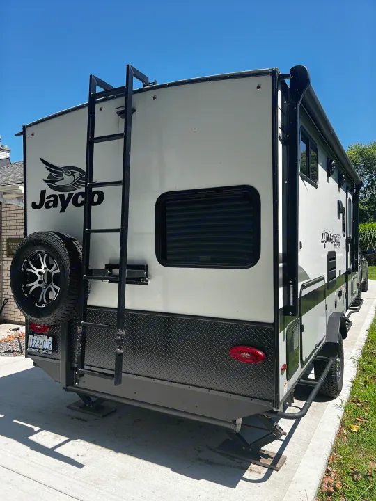 A sleek white and black Jayco RV travel trailer, ideal for an RV rental adventure. Features a rear ladder, spare tire, and tinted windows.. Jayco Jay Feather Micro 2022