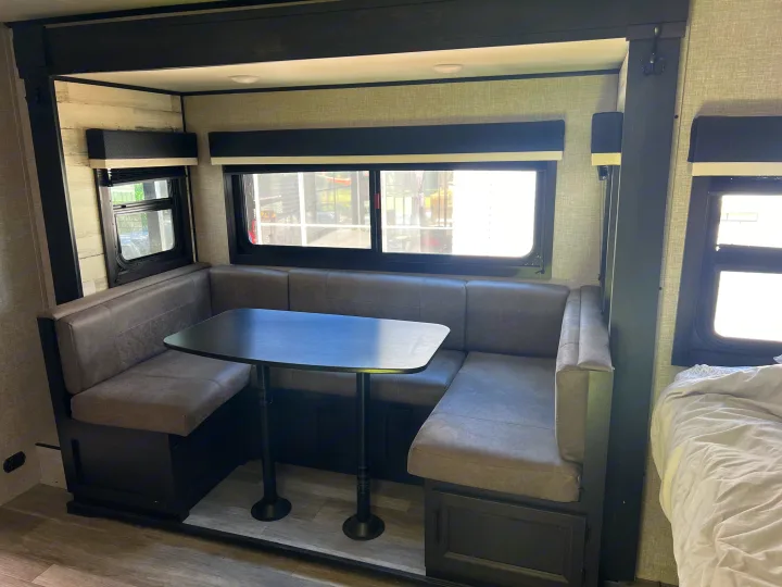 Inside an rv rental, showing the cozy U-shaped dinette with grey cushions and dark table for comfortable travel and dining.. Jayco Jay Feather Micro 2022