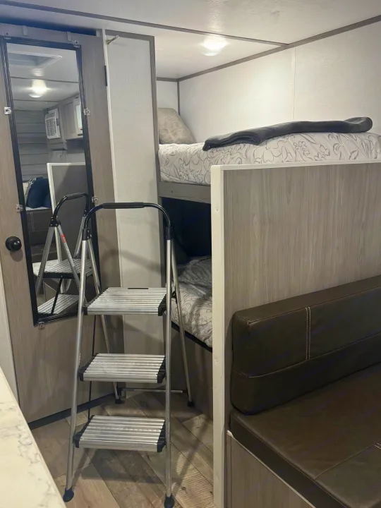 RV rental interior featuring bunk beds, a step ladder, and a full-length mirror, optimizing compact living space.. Coleman Lantern LT 17B 2024