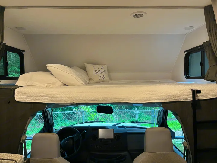 This rv rental features a cozy cabover bunk bed with white bedding, above the driver's cockpit. Ideal for your next adventure.. Forest River Solera 27 DSE 2023