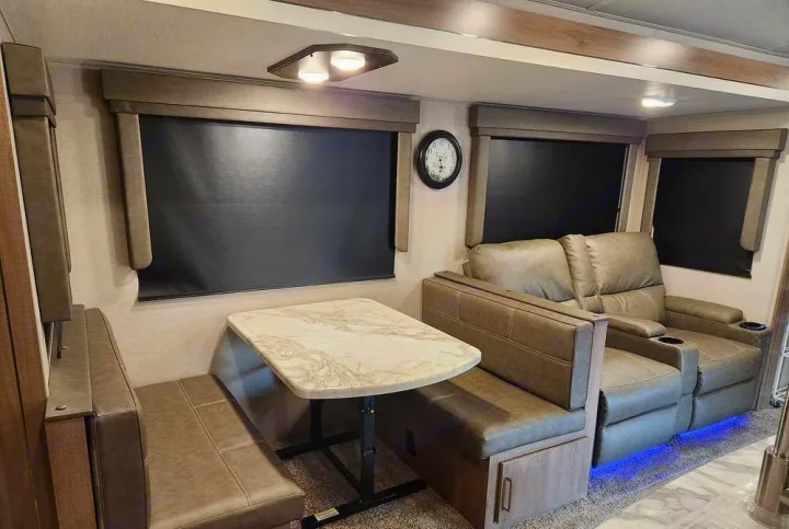This RV rental features a comfortable dinette with a marble table and plush recliners, creating a cozy living and dining space.. Grand Design Imagine 2023