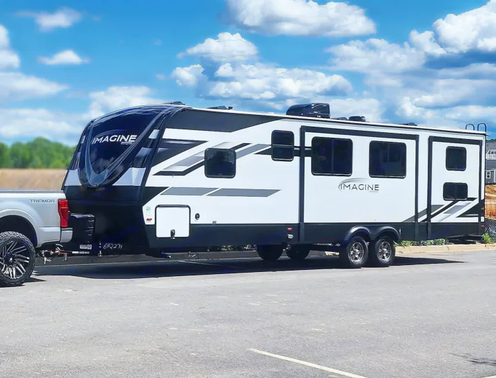A sleek black and white Imagine RV travel trailer hitched to a Ford Tremor pickup truck, ready for rv rental adventures.. Grand Design Imagine 2023