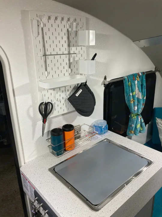 Compact RV rental kitchen features white pegboard storage, Yeti tumblers, and covered sink for efficient use of space.. Helio Helio Trailer 2023