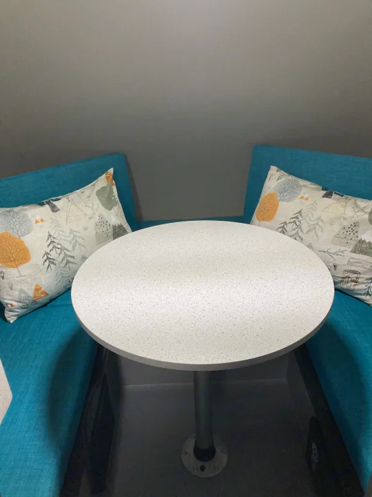 RV rental interior: Cozy dining booth with a white speckled table and blue seats with nature-themed pillows.. Helio Helio Trailer 2023