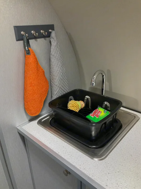 Functional kitchen in an RV rental: Sink with a dish rack, scrub brush, sponge, and two towels on hooks.. Helio Helio Trailer 2023