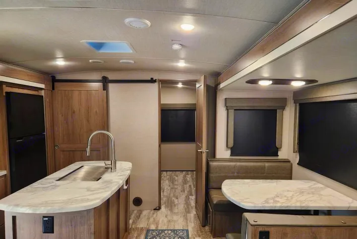Spacious RV rental interior showcasing a modern kitchen island with sink, dining booth, and hallway leading to private quarters.. Grand Design Imagine 2023
