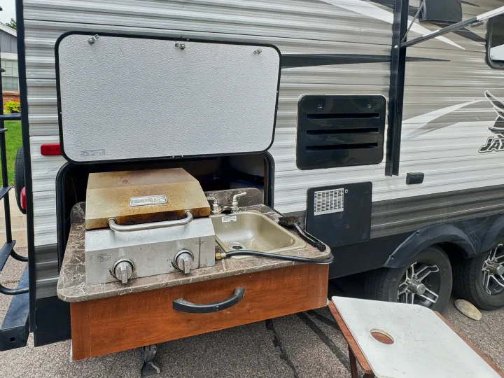 An RV rental's outdoor kitchen, featuring a grill, sink, and counter, extends from this travel trailer, ready for use.. Jayco Jay Flight 2014