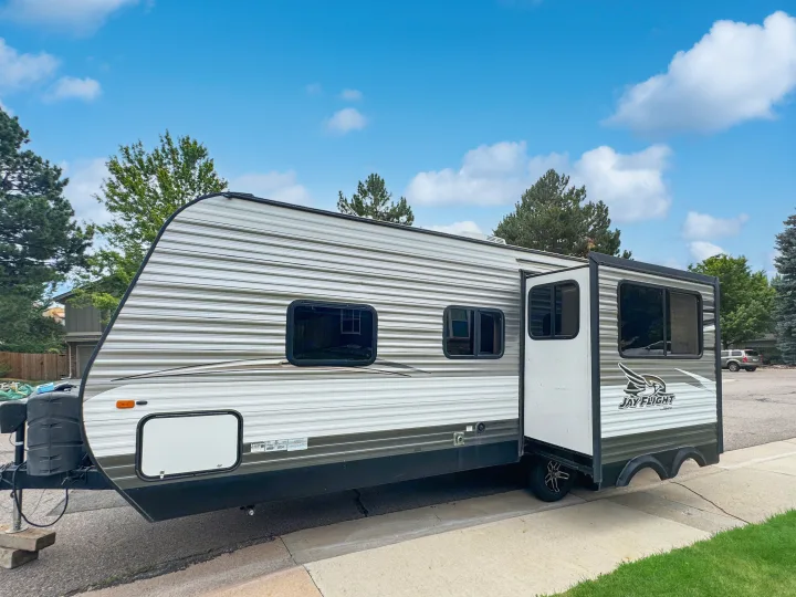 A large white and gray striped Jay Flight travel trailer, ideal for an rv rental, is parked with its slide-out extended.. Jayco Jay Flight 2014