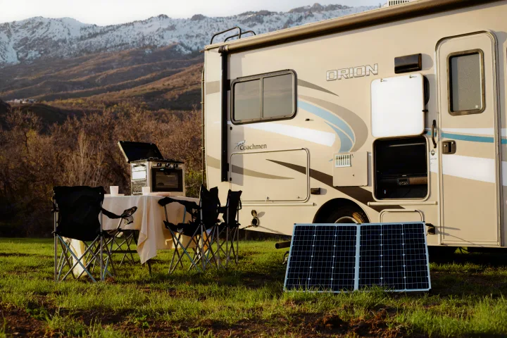 RV rental adventure: Coachmen Orion RV with portable solar panel, outdoor grill, and dining setup against mountains.. Coachmen Orion 2020