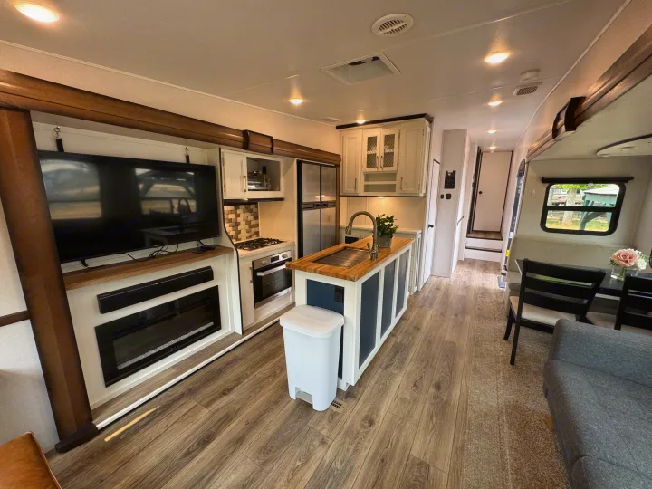 Modern RV rental interior: fully equipped kitchen with island, living room with TV & fireplace, and dining area.. Prime Time Crusader 2021