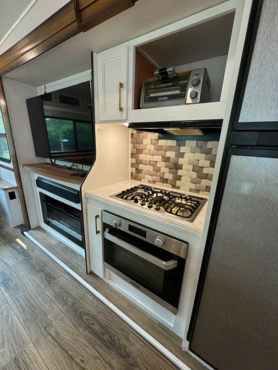 Clean rv rental interior featuring a full kitchen with stove, oven, toaster, fridge, and a living area with TV & fireplace.. Prime Time Crusader 2021