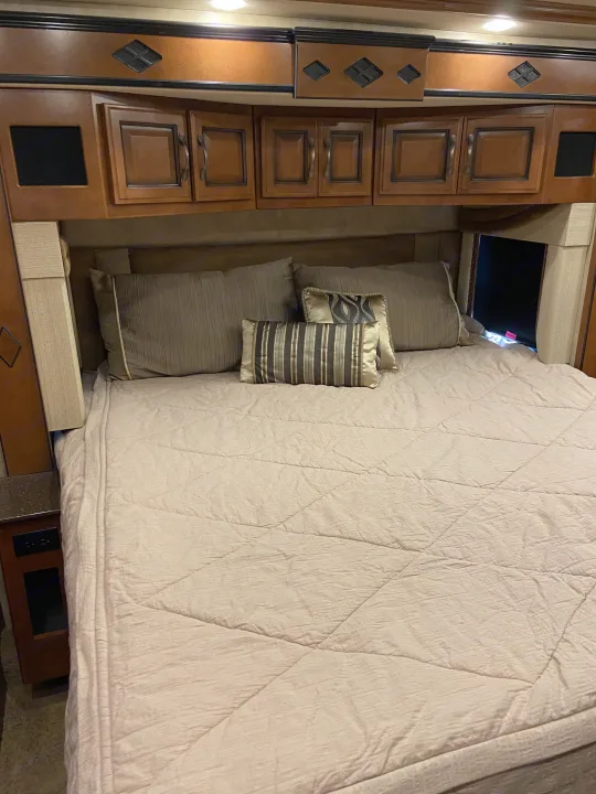 RV rental bedroom: a cozy bed with decorative pillows and functional wooden overhead cabinets, complete with accent lighting.. Fleetwood Other 2015