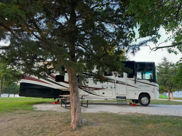 Spacious RV rental parked at a serene lakeside campsite with a picnic table and trees.. Georgetown Georgetown Motorhome 2016