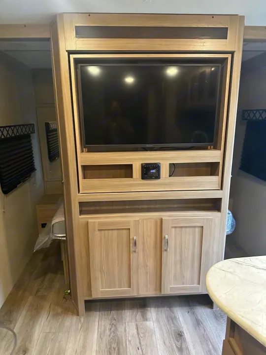 Bright RV rental interior with entertainment center, TV, and stereo, showcasing light wood cabinetry and bed area.. Coachmen fet257bhs-320 2021