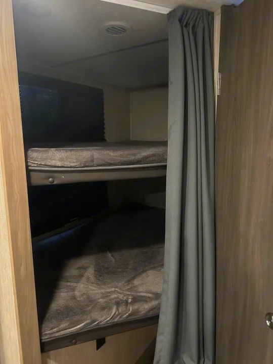 View inside an RV rental showing stacked bunk beds with dark mattresses and a gray privacy curtain. A compact sleeping area.. Coachmen fet257bhs-320 2021